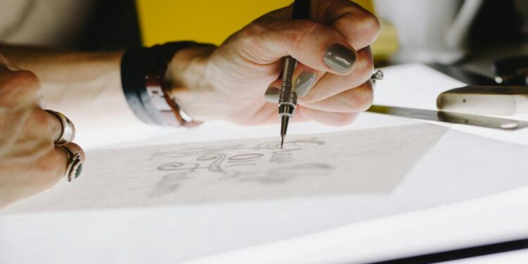 person lettering on tracing paper using mechanical pencil